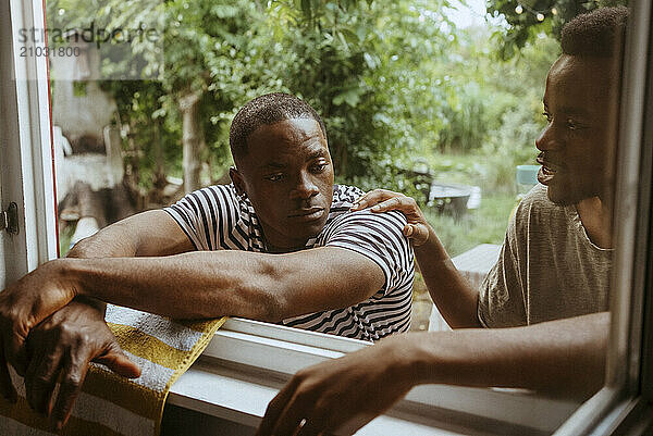 Man consoling male friend while keeping hand on shoulder seen through window glass