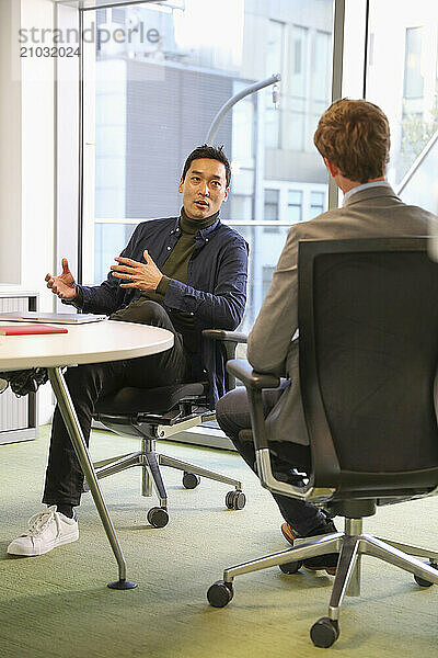 Businessmen talking in office; Two businessmen talking at table in modern office