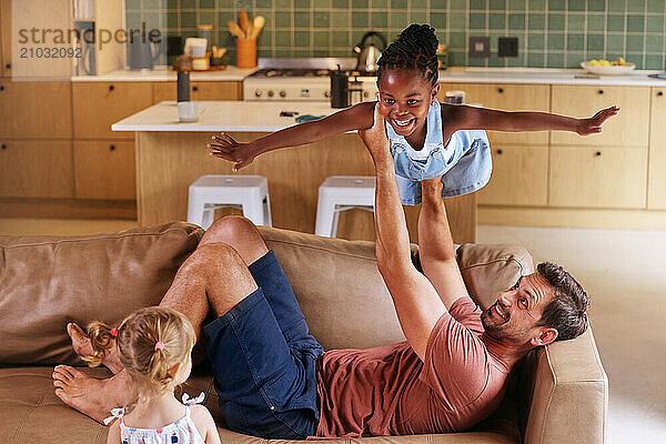 Father playing with daughters (18 - 23 months  6-7) on sofa