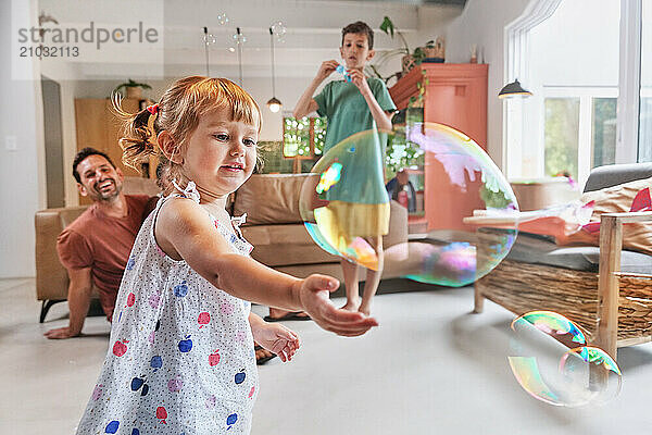 Father with children (18 - 23 months  6-7  8-9) playing with bubbles