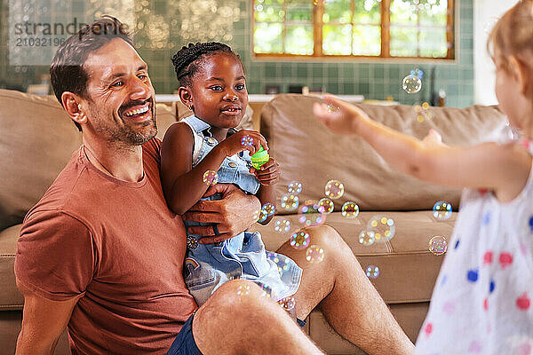 Father with daughters (18 - 23 months  6-7) playing with bubbles