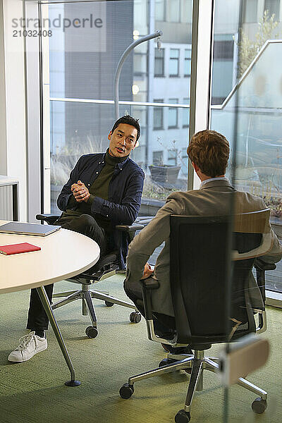 Businessmen talking in office; Two businessmen talking at table in modern office