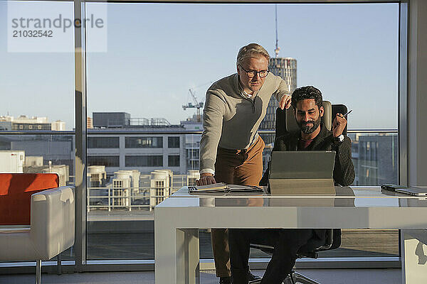 Businessmen talking in office; Two businessmen looking at digital tablet and talking in modern office at desk