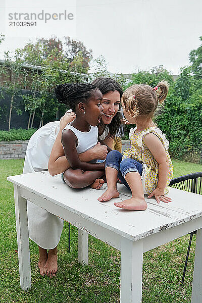 Mother with daughters (18-22 months  6-7) playing on back yard