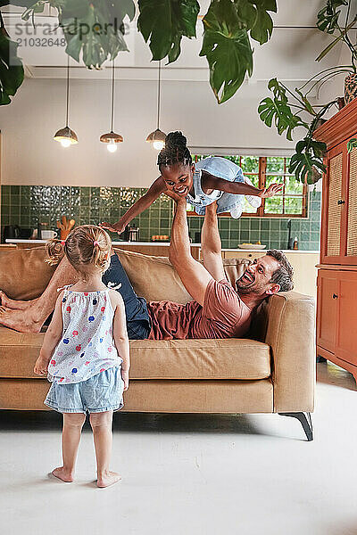 Father playing with daughters (18 - 23 months  6-7) on sofa