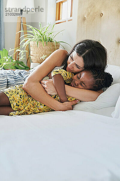 Mother hugging daughter (6-7) on bed