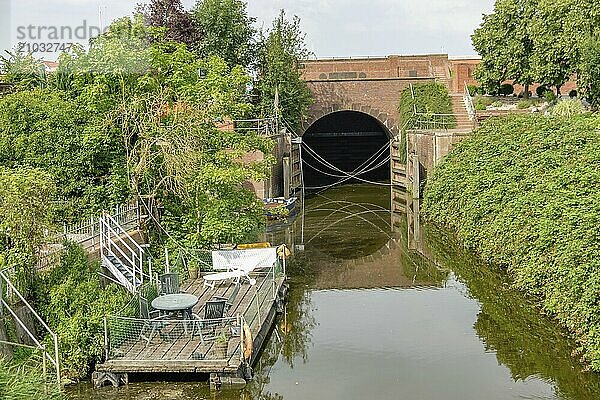 Waterway passing under a bridge  surrounded by green vegetation and small boats  ditzum  east frisia  germany