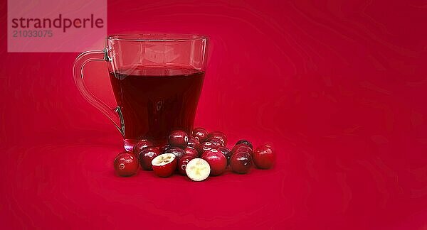 Red cranberries and transparent cup containing a dark red cranberry juice against a vibrant red background