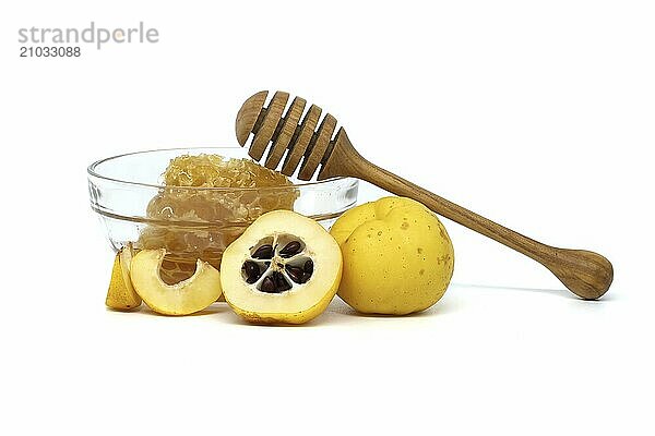 Glass bowl brimming with honey and wooden dipper resting on its rim surrounded by vibrant quince fruits  both sliced and whole isolated on white background  full depth of field