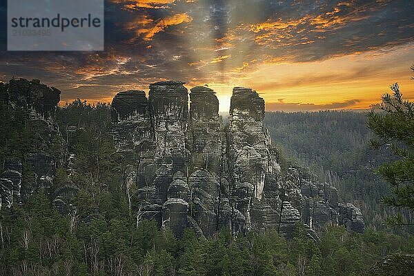 Rugged rocks at Basteibridge at sunset. Wide view over trees and mountains. National park in Germany