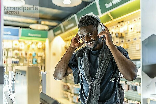 Happy African young man buying headphones in electronics store