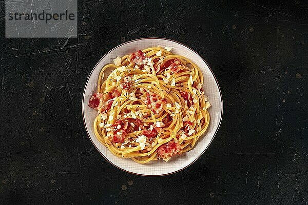 Carbonara pasta dish  traditional Italian spaghetti with pancetta and cheese  overhead flat lay shot on a black background  Food photography