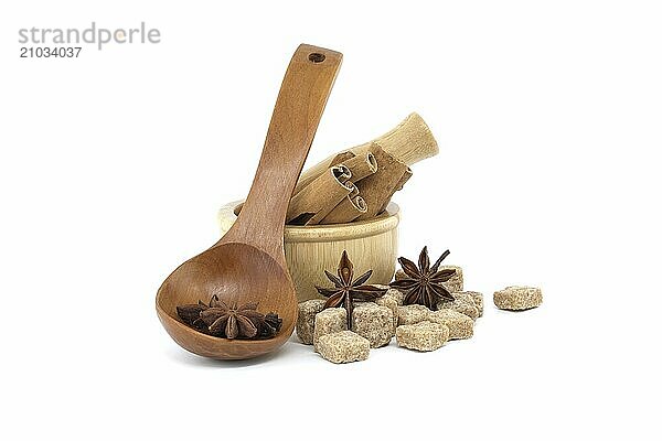 Star anise in a wooden spoon  wooden mortar filled with cinnamon sticks and brown sugar cubes isolated on white background