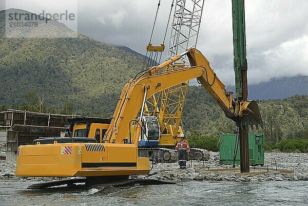 Builders use a digger to straighten the pylons for a concrete bridge over a small river in Westland  New Zealand  Oceania