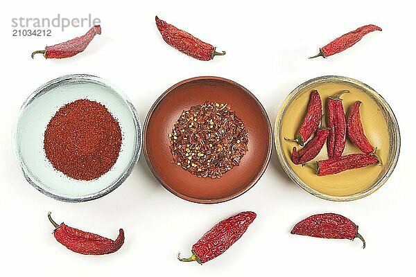 A flatlay photo of wooden bowls with whole peppers  red pepper powder  and red pepper flakes against a white background