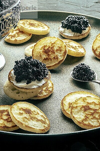 Blinis with black caviar  on a festive dish on a black background  mini pancakes  an elegant appetizer  Food photography  Food photography