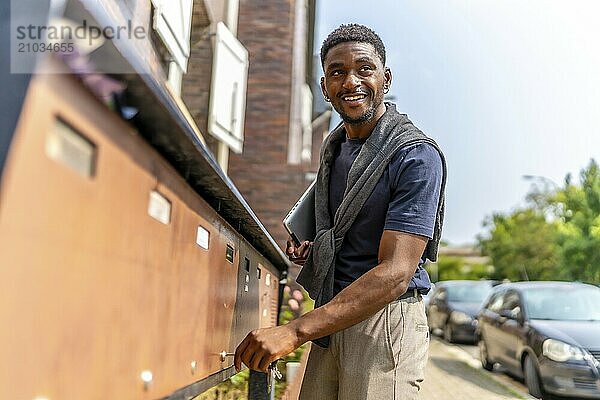 Side view three quarter length photo of a happy and confident african young man checking mailbox in the street