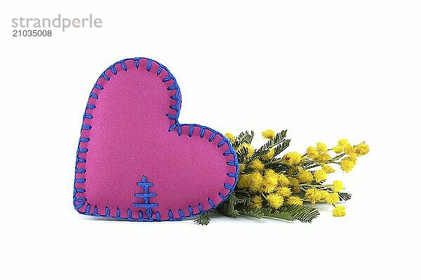 Lovely heart-shaped vibrant shade of pink pillow beside captivating display of yellow mimosa flowers isolated on white background