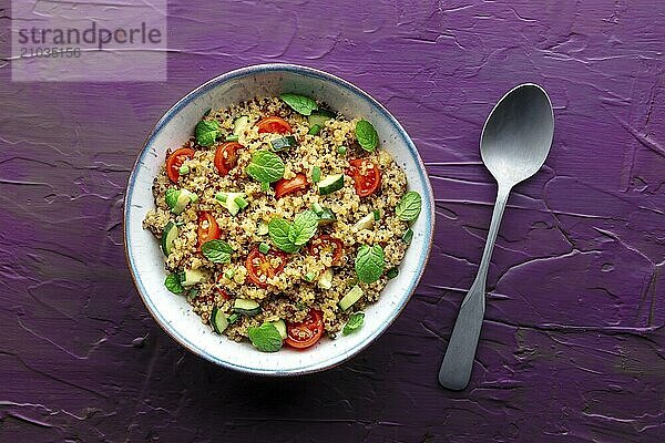 Quinoa tabbouleh salad in a bowl  a healthy dinner with tomatoes and mint  with a spoon  top shot on a purple background  Food photography