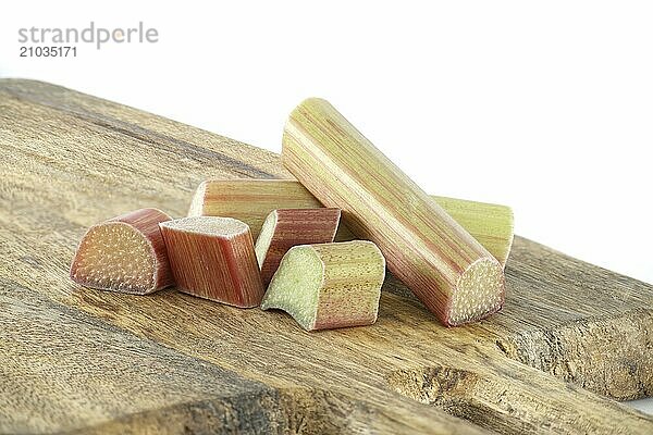 Rhubarb stalks of varying colors from pale green to deep red on wooden cutting board isolated on white background