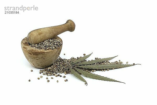 Hemp seeds in wooden rustic-style mortar near pestle and cannabis plant leaf isolated on white background