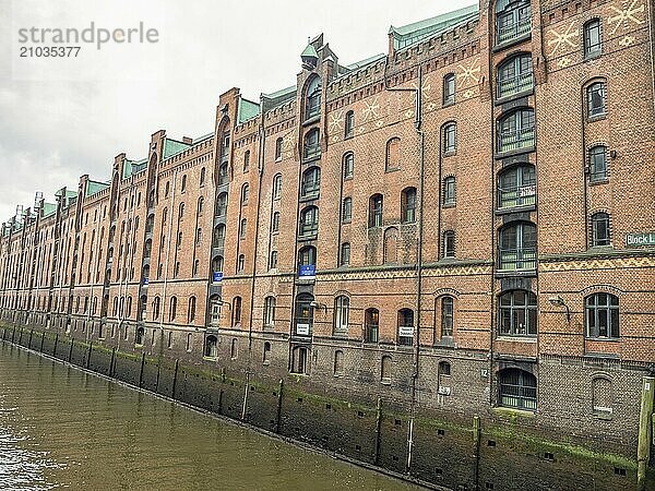 Historic brick building with many windows and decorative details along a canal on a cloudy day  Hamburg  Germany  Europe