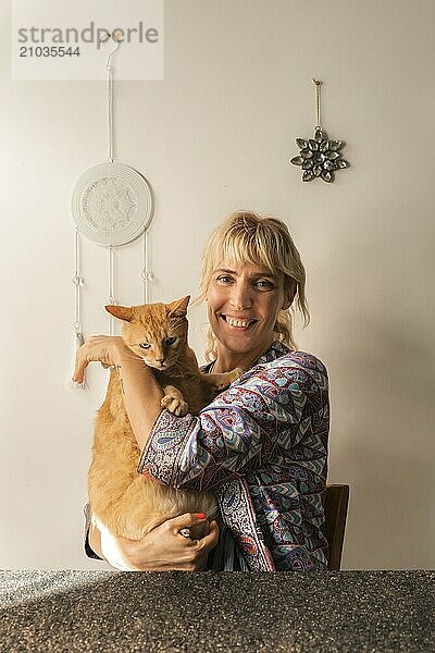 Smiling woman looking at the camera with her beautiful cat in her lap