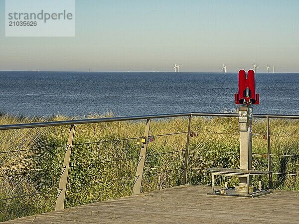 A red telescope on a platform with a view of the sea and wind turbines in the background  egmond aan zee  the netherlands