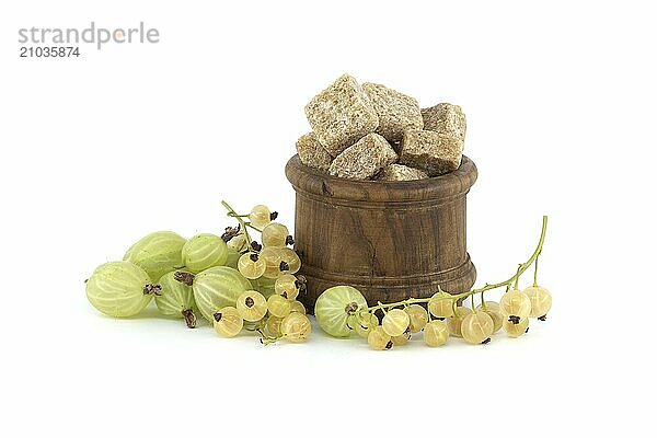 Gooseberries and yellow currants next to brown cane sugar cubes in wooden bowl  isolated on white background  berry jam  compote preparation