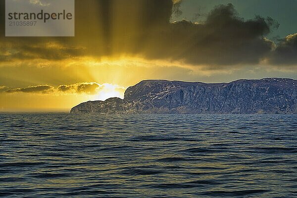 View from the sea to the West Cape in Norway in sunshine and heavy clouds. Waves in the foreground  rocks in the background. Westernmost point of Europe