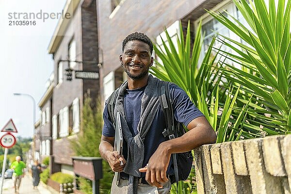 Portrait of a confident african entrepreneur holding laptop standing next to a house in a residential district