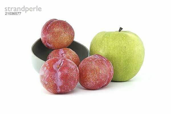 Collection of fresh fruits comprising red plums and bright green apple arranged against a white background