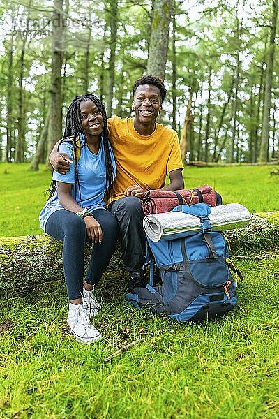 Vertical portrait of young african friends embracing sitting on a log together in a green forest in spring