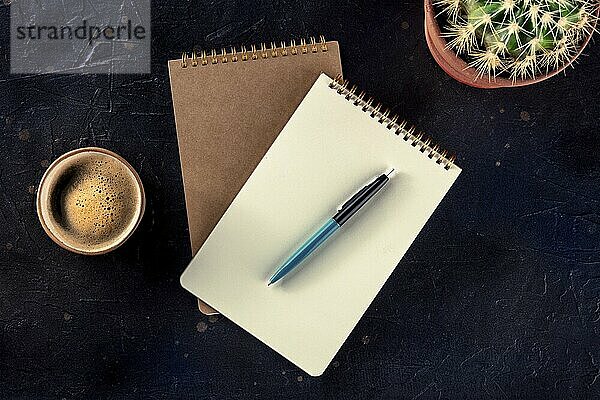 Notebook with a pen  coffee  and plant  overhead flat lay shot on a black background  a mockup  Food photography