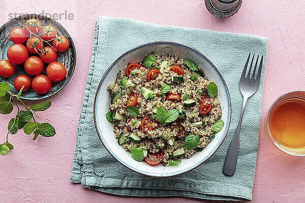 Quinoa tabbouleh salad in a bowl  a healthy dinner with tomatoes and mint  overhead flat lay shot on a pink background  Food photography  Food photography