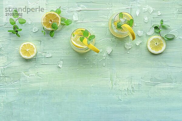 Lemonade with mint. Lemon water drink with ice. Two glasses and lemons on a blue background  shot from the top with a place for text. Detox beverage. Fresh homemade cocktail