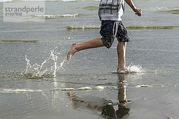 Boy runs along beach and makes splashes in the water at Pacific Beach in Washington