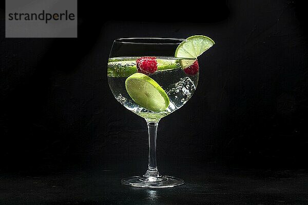 Fancy cocktail with fresh fruit. Gin and tonic drink with ice at a party  on a black background. Alcohol with lime and raspberry  Food photography  Food photography