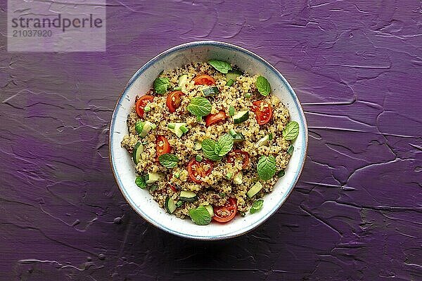 Quinoa tabbouleh salad in a bowl  a healthy dinner with tomatoes and mint  overhead shot on a purple background  Food photography  Food photography