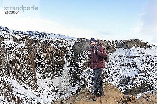 Portrait of a hiker at frozen Hengifoss waterfall in cold Iceland winter  volcanic cliffs