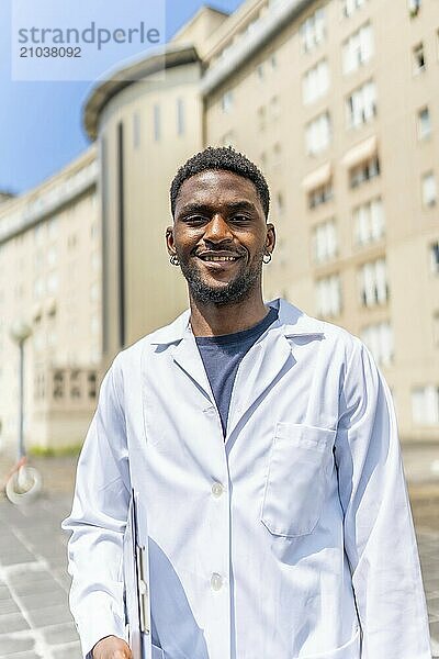 Vertical portrait of a cheerful african doctor smiling at camera outside the hospital