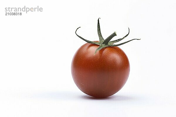 A ripe cherry tomato with a green stem stands on a white background in this studio photo