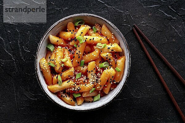 Tteokbokki or topokki  Korean street food  spicy rice cakes in red pepper gochujang sauce  shot from the top with chopsticks on a black background  Food photography