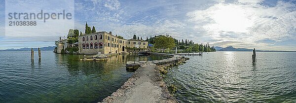 A serene view of a historic lakeside building by a calm lake with a pier extending into the water  surrounded by trees and mountains under a clear sky  Locanda San Vigilio  Punta San Vigilio  Garda  Lake garda  Lago di Garda  Veneto  Italy  Europe