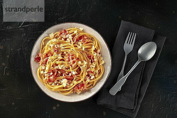 Carbonara pasta dish  traditional Italian spaghetti with pancetta and cheese  overhead flat lay shot with a fork and a spoon  on a black background  Food photography