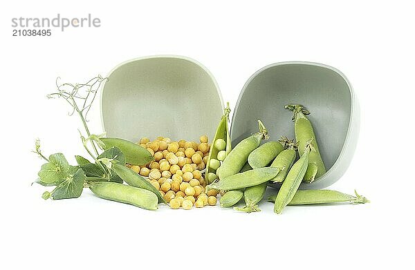 Dried yellow peas spilling out from bowl and fresh garden peas pods with green leaves isolated on a white background