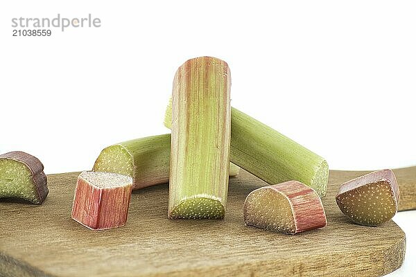 Variety of rhubarb stalks of varying colors from pale green to deep red on wooden cutting board isolated on white background