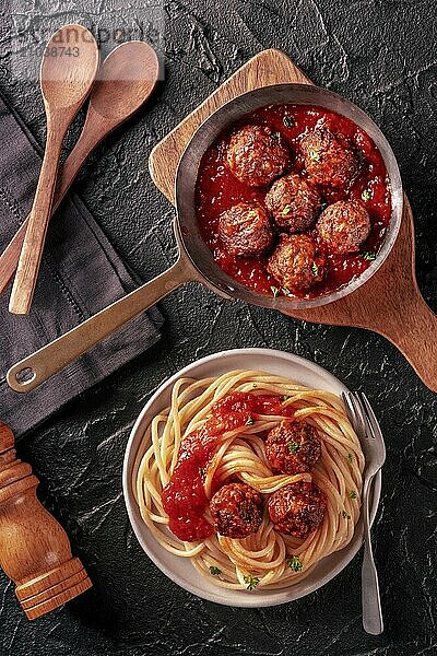 Meatballs. Beef meat balls  overhead flat lay shot in a pan and with a plate of spaghetti pasta  on a black background  with wooden spoons