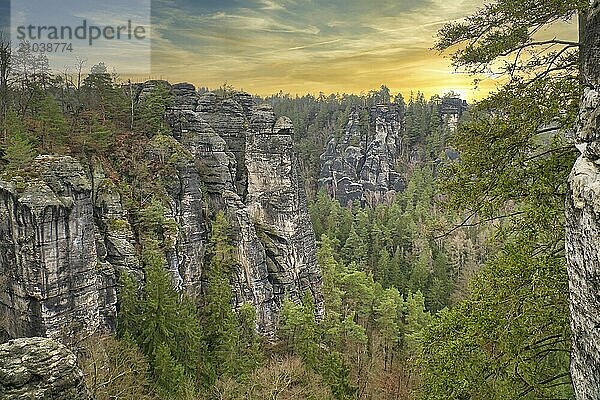 Rugged rocks at Basteibridge at sunset. Wide view over trees and mountains. National park in Germany