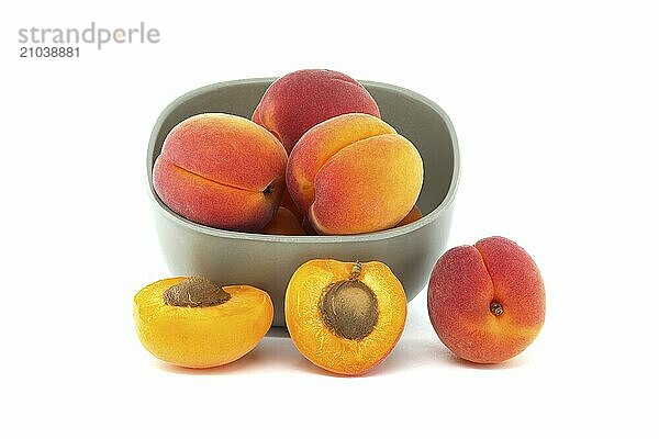 Bowl filled with fresh whole apricots and one cut in half to reveal its interior  isolated on a white background